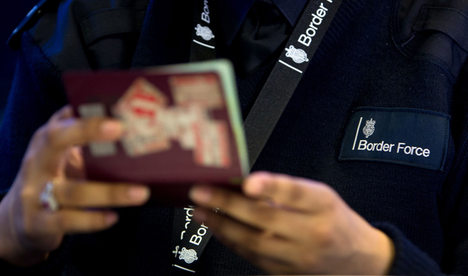 Image shows a UK Border Force official checking a passport