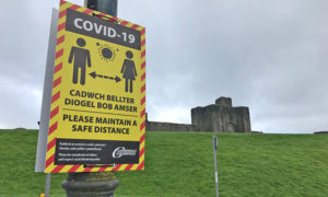 A social distancing warning sign near Caerphilly Castle