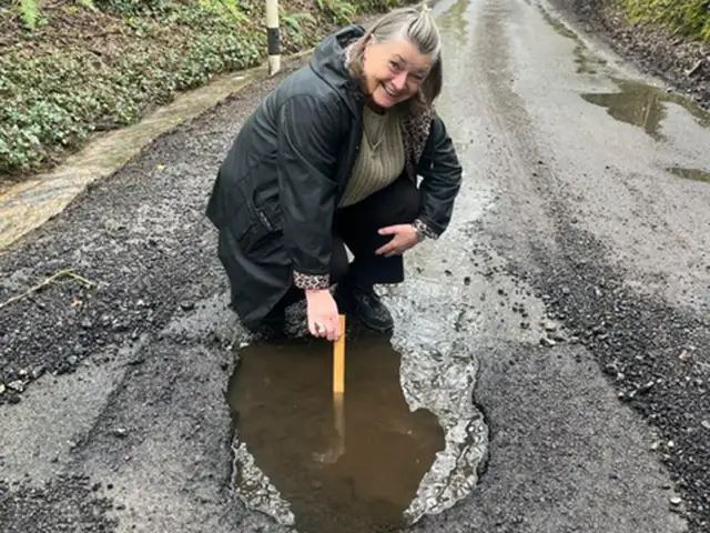 Mair Arthur, the landlady of the White Cross Inn, measuring the depth of a pothole in Groeswen Lane